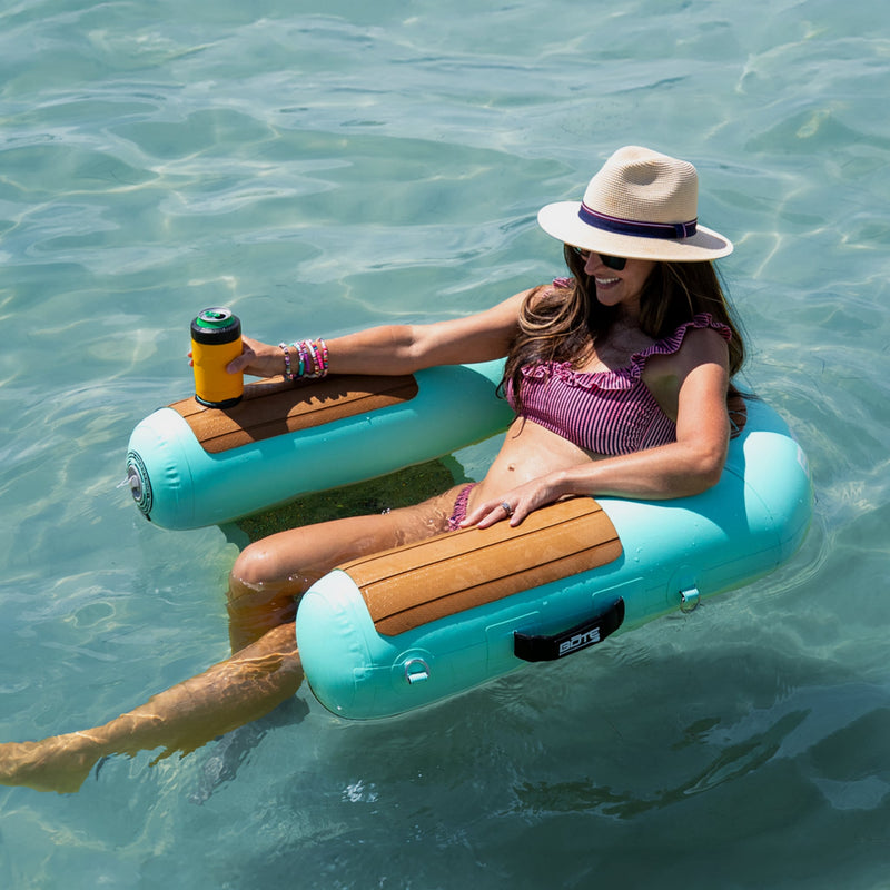 A woman lounging in a BOTE Hangout Inflatable Sling Chair with a drink.